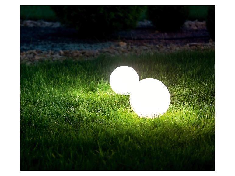 Zwei leuchtende kugelförmige Gartenleuchten auf grünem Gras bei Nacht