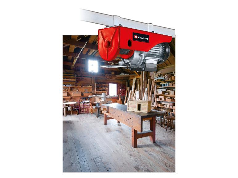Roter Elektrozug in einer rustikalen Holzwerkstatt mit Werkzeugen und Holzarbeitsbänken.
