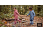 Kinder in Regenanzügen und Gummistiefeln spielen in einer Pfütze im Wald.