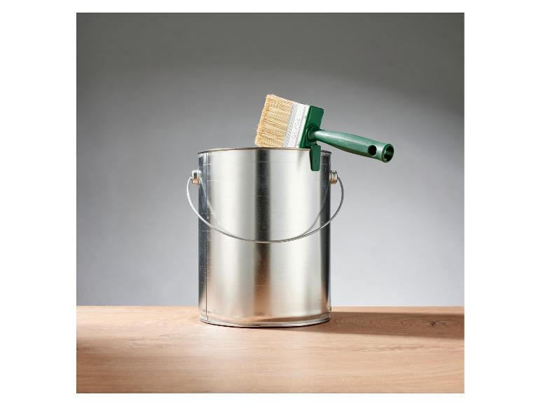 Grüner Pinsel lehnt an einer Metallfarbdose auf einem Holztisch.