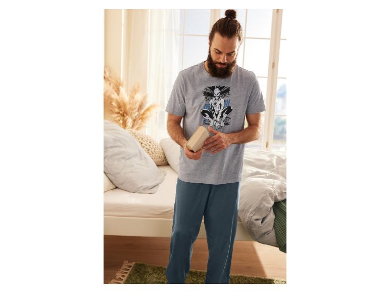 Mann in einem grauen Pyjama mit Spiderman-Druck und blauen Hosen, hält ein Buch.