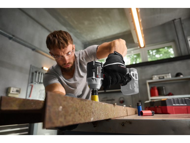 Mann mit Schutzbrille benutzt einen Schlagschrauber an einem Metallträger.