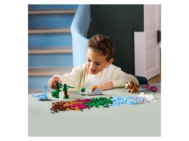 Kind spielt mit LEGO Duplo Dinosauriern und Vulkan auf einem Tisch.