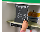 Kinderhand, die mit Kreide auf eine Tafel in einer Spielzeugküche zeichnet.