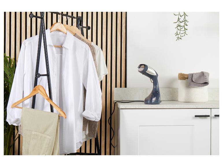 Dampfglätter auf einer Arbeitsplatte neben einem Kleiderständer mit Hemden und Hosen.