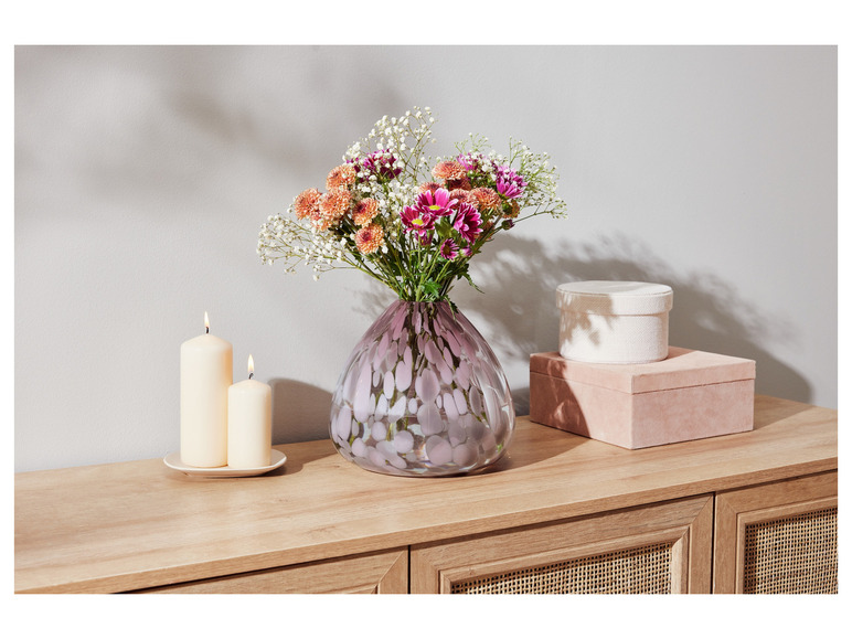 Blumen in einer Glasvase mit Punkten auf einer Kommode aus Holz mit zwei Kerzen und zwei Schachteln.