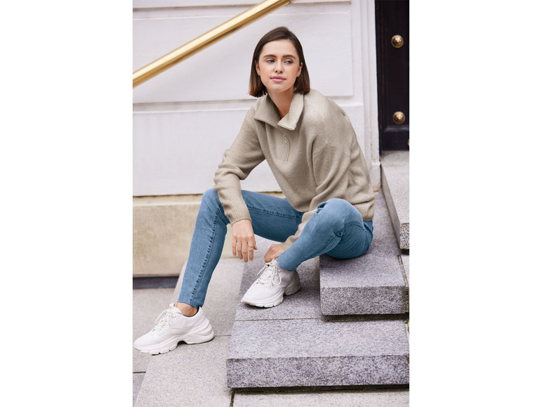 Eine Frau in einem beigen Pullover und blauen Jeans sitzt auf Stufen.