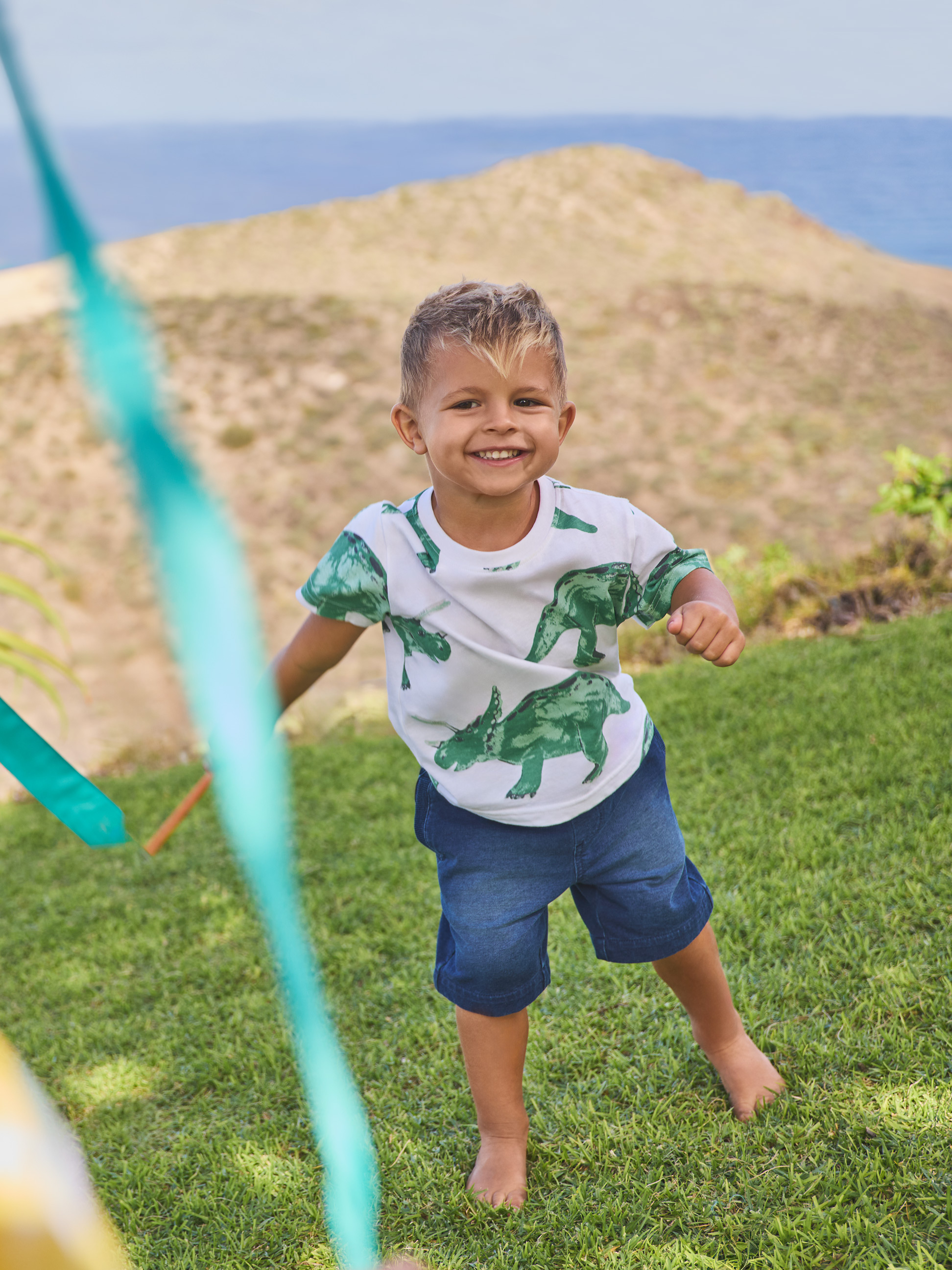 Junge in Dinosaurier-T-Shirt und Jeans-Shorts, spielt draußen.
