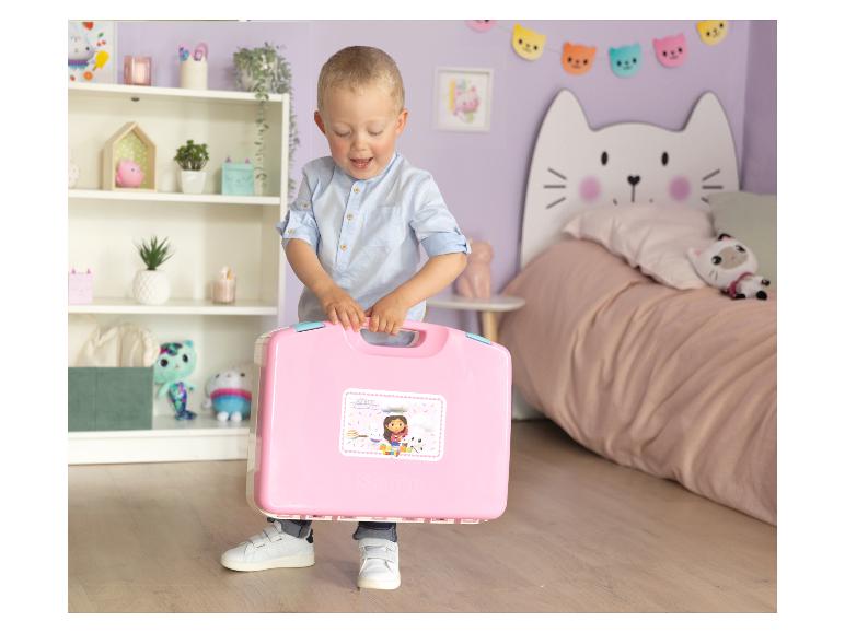 Ein Junge hält einen pinken Gabby's Dollhouse Spielzeugkoffer in einem Kinderzimmer.
