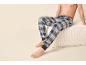 Oberkörperfreier Mann in blau-weiß karierter Pyjamahose, sitzt auf einem weißen Hocker.