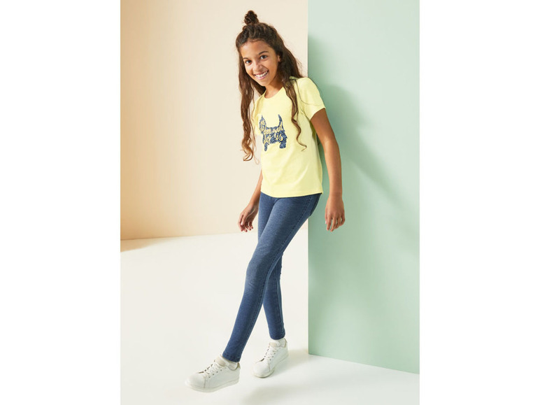 Ein Mädchen trägt ein gelbes T-Shirt mit Hundeaufdruck und blaue Jeans.