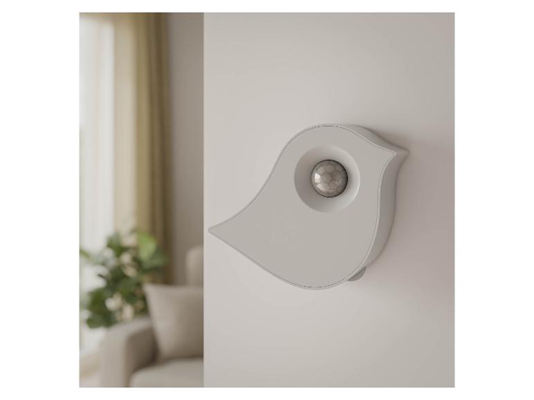 Weißer vogelförmiger Bewegungssensor an der Wand in einem Wohnzimmer.