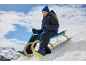 Mädchen in blauem Schneeanzug und Mütze, auf einem Holzschlitten im Schnee sitzend.