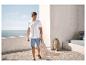 Mann in weißem Poloshirt und Jeans-Shorts auf einer Terrasse mit Meerblick.