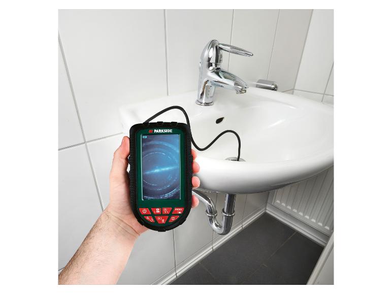 Ein Mann hält eine Parkside Inspektionskamera für Rohre, während er einen Abfluss eines Waschbeckens inspiziert.