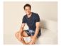 Mann in marineblauem T-Shirt und karierten Shorts, sitzt auf einem beigen Sofa.
