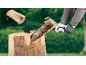 Person spaltet Holz mit einer Axt auf einem Hackklotz, Holzsplitter fliegen weg.