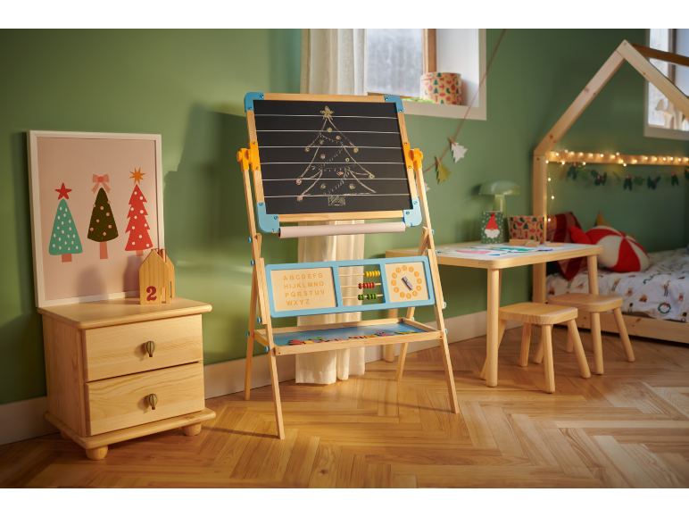Kinderzimmer mit Holzstaffelei, kleinem Tisch mit Hockern und Bett, weihnachtlich dekoriert.