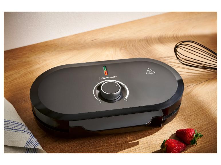 Schwarzes SilverCrest Waffeleisen auf Holzoberfläche mit Erdbeeren und Schneebesen.