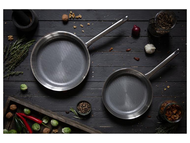 Zwei antihaftbeschichtete Pfannen, umgeben von frischen Kräutern und Gemüse.