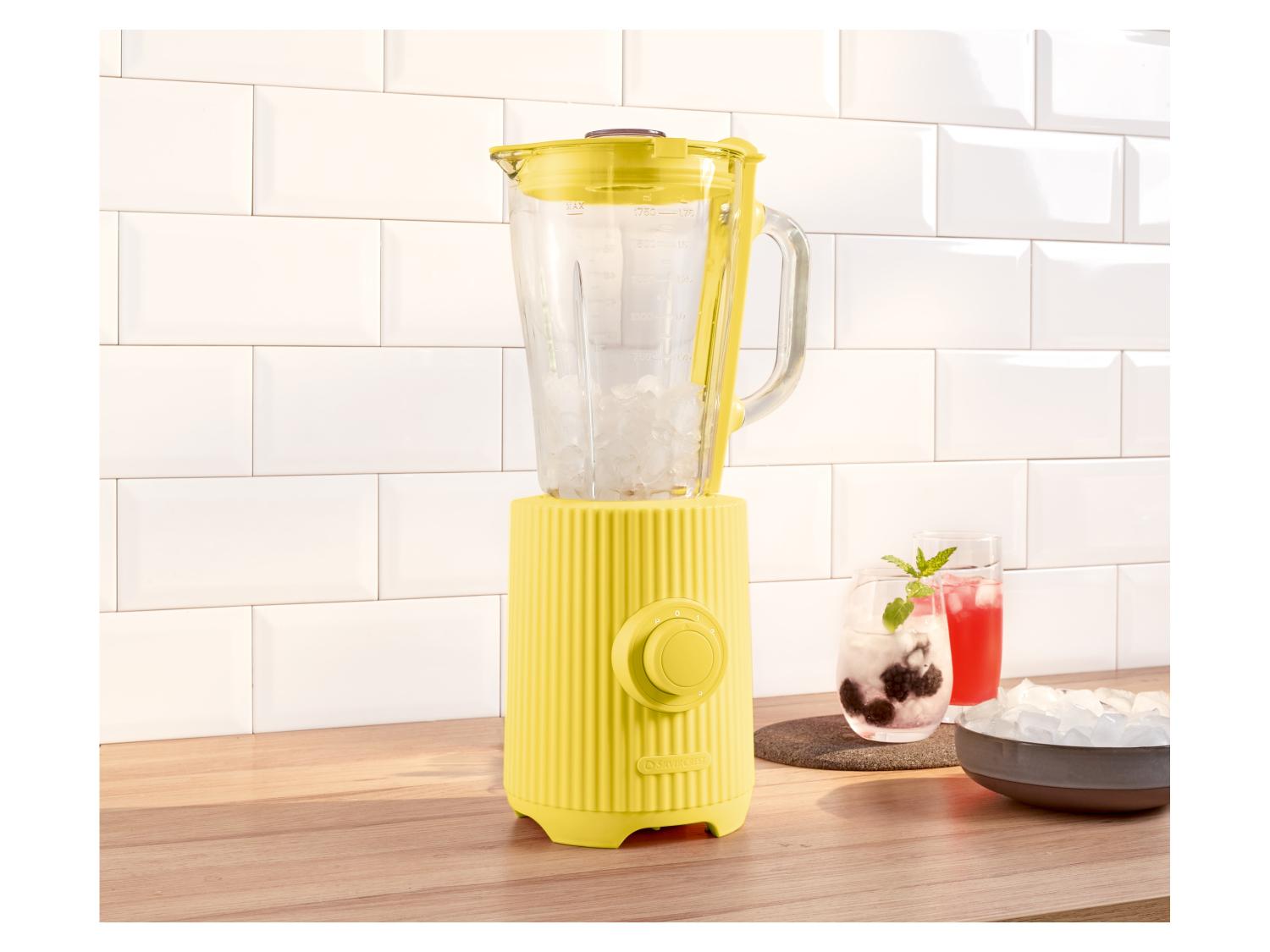 Gelber SilverCrest Mixer mit Eis, Getränken und einer Eisschale auf einer Küchenarbeitsplatte.
