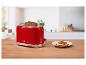 Roter Toaster mit zwei Brotscheiben und einem Teller mit Tomatenbrot in einer Küche.
