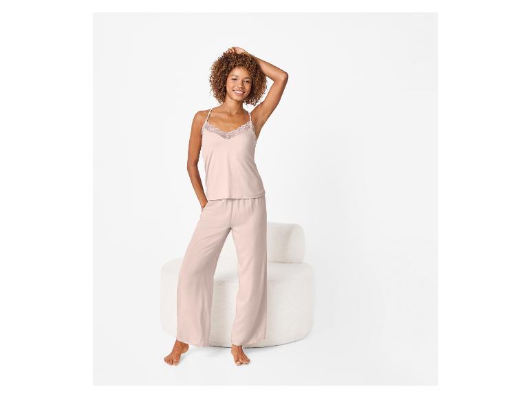 Frau in rosa Pyjama mit Spitzentop, stehend neben einem weißen Sessel.