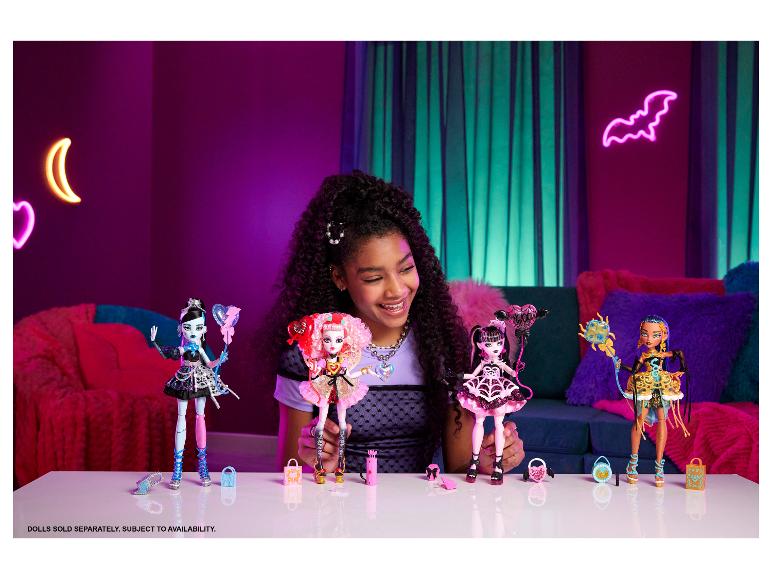 Ein lächelndes Mädchen hält Monster High Puppen, mit weiteren Puppen und Accessoires auf einem Tisch.