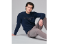 Mann in dunkelblauem Pullover mit Schriftzug und grauer Hose, sitzend auf grauem Hintergrund.