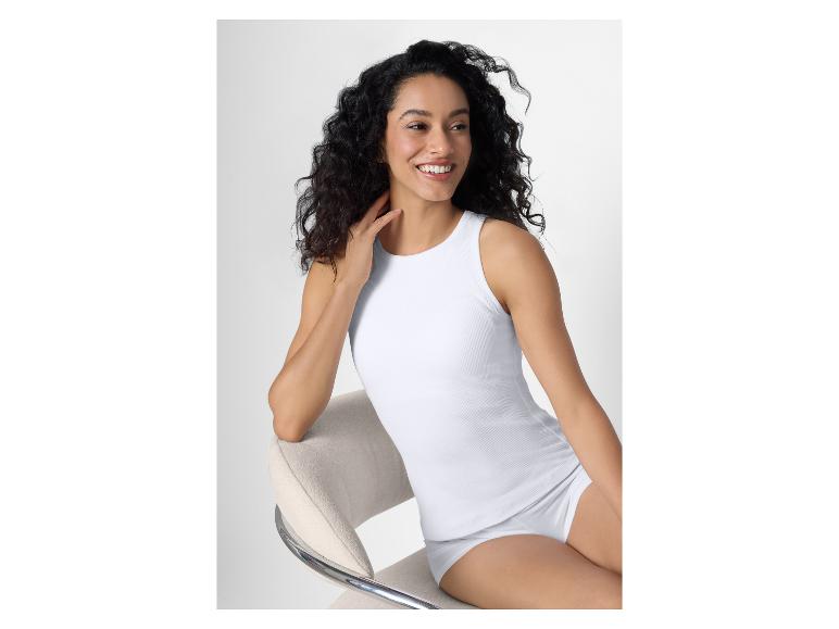 Frau in weißem Ripp-Tanktop und Slip, auf einem Stuhl sitzend.