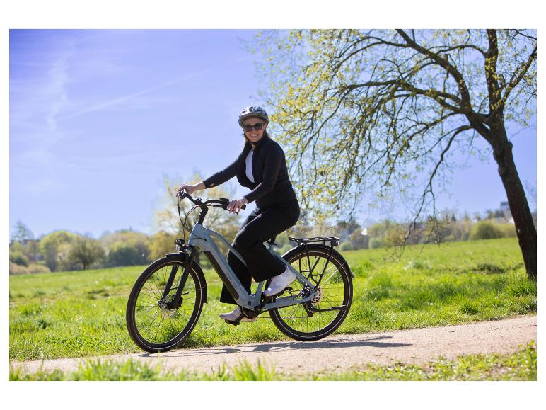 Frau mit Helm und Sonnenbrille auf einem E-Bike auf einem Feldweg.
