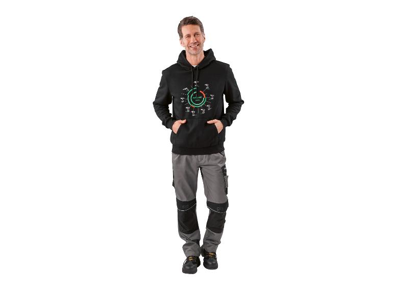 Mann in schwarzem Kapuzenpullover und grauer Arbeitshose, mit Bohrmaschinen-Evolution auf dem Pullover.