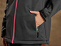 Eine schwarze Softshelljacke mit rosafarbenem Reißverschluss und einer Reißverschlusstasche.
