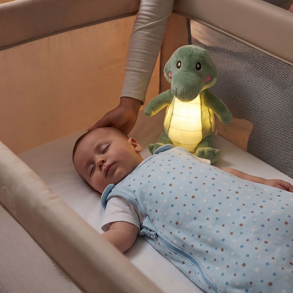 Baby schläft im Kinderbett mit leuchtendem Krokodil-Nachtlicht und einer Hand, die sanft den Kopf berührt.