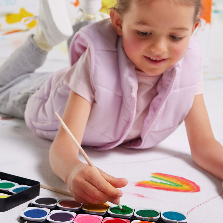 Mädchen malt Regenbogen mit Wasserfarben und Pinsel auf Papier.