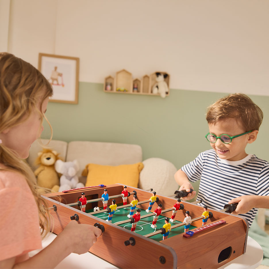Zwei Kinder spielen Tischfußball, Mädchen links, Junge rechts.