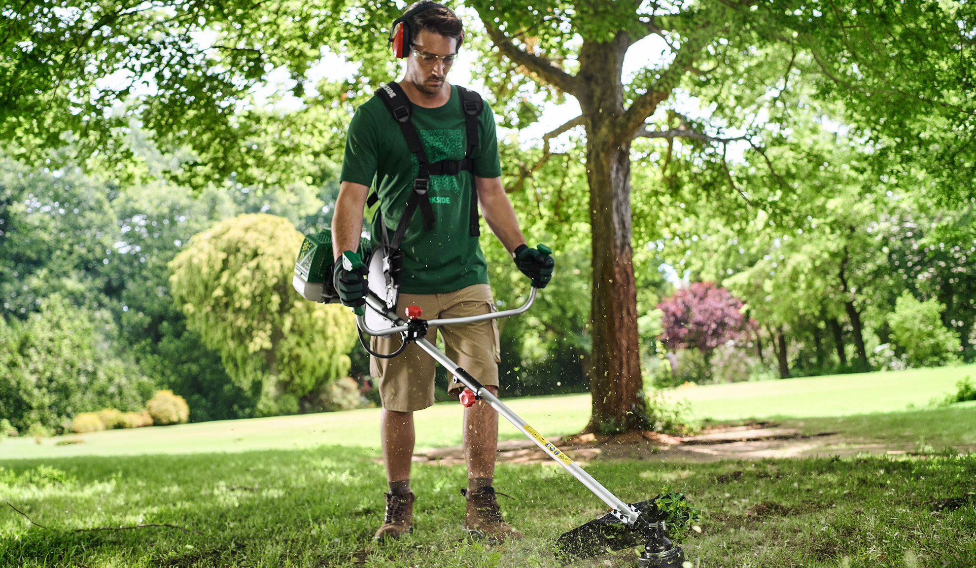 Mann trimmt Gras im Garten mit einem Freischneider, trägt Schutzbrille und Gehörschutz.