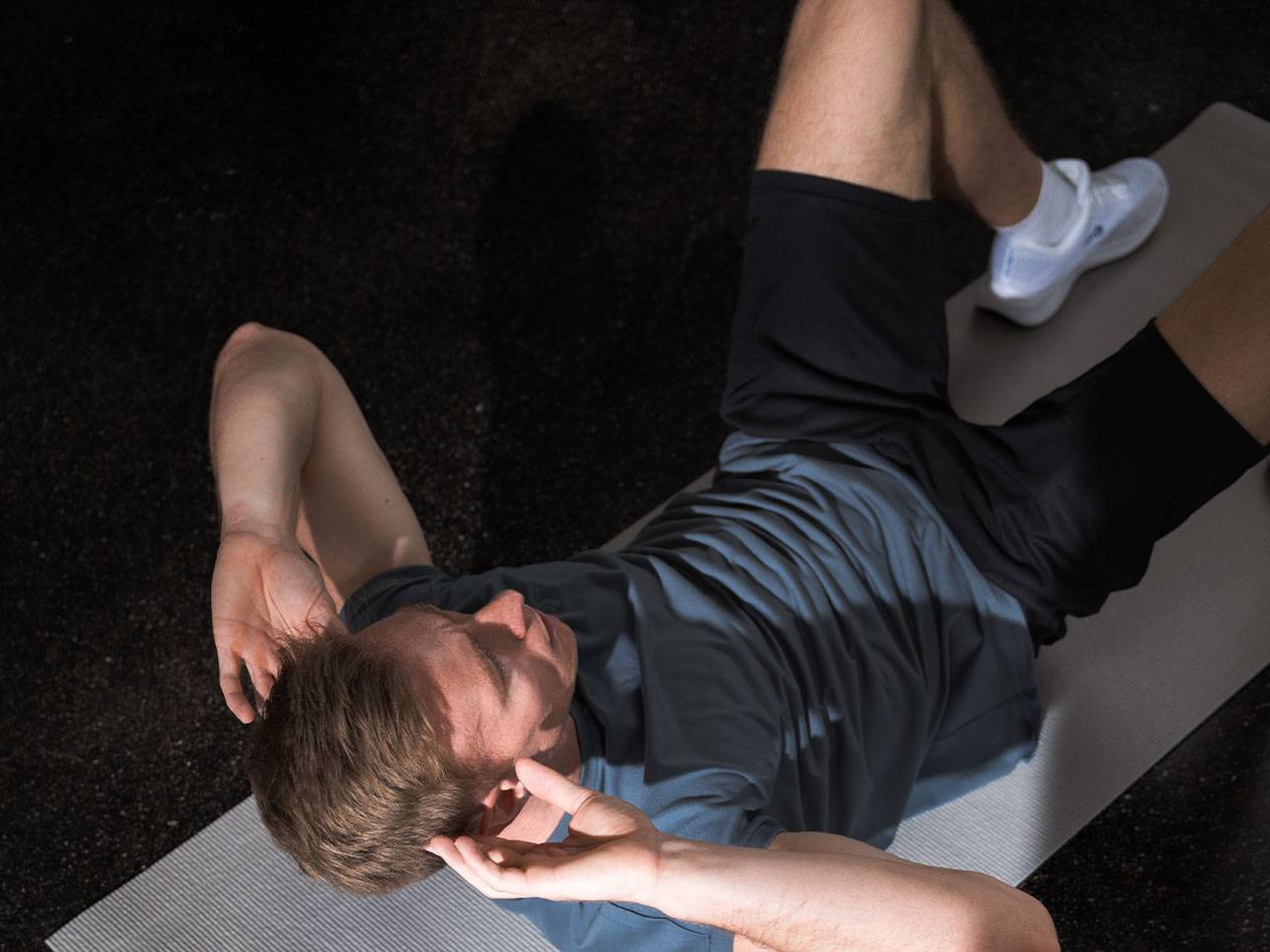 Mann in blauem T-Shirt und schwarzen Shorts macht Crunches auf einer Yogamatte.