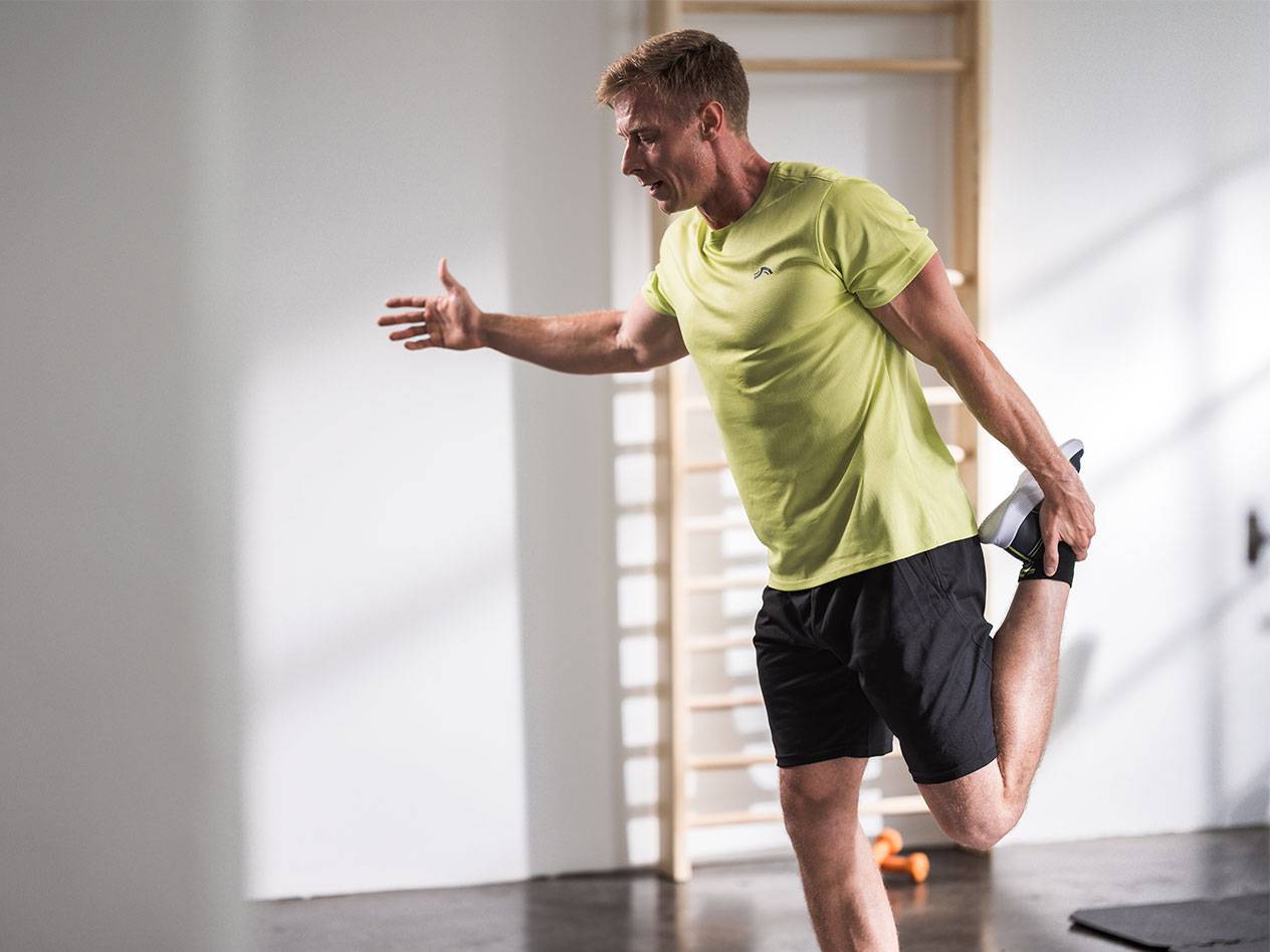 Mann dehnt sich in schwarzen Shorts und einem lindgrünen T-Shirt in einem Fitnessstudio.