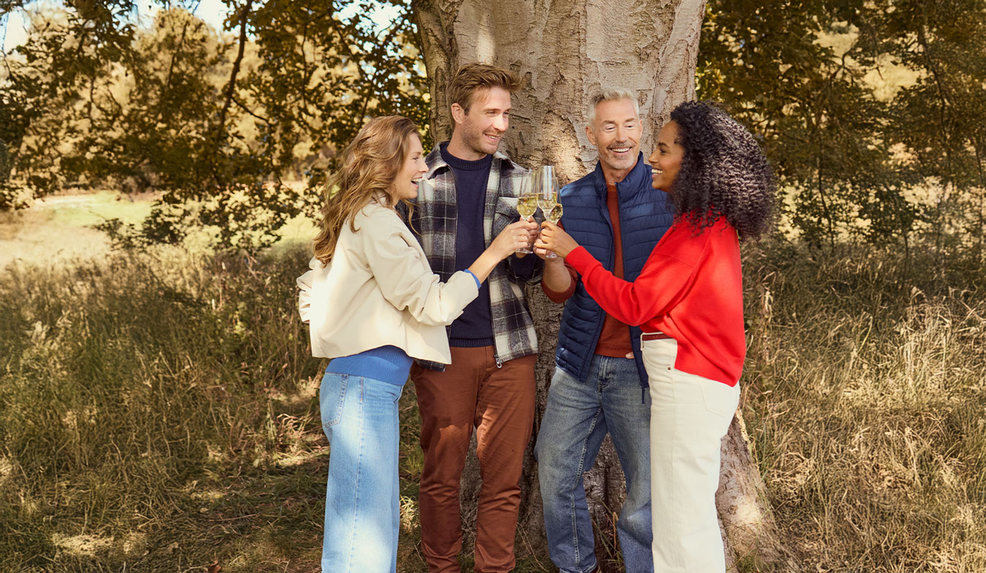 Vier Freunde in lässiger Herbstkleidung stoßen draußen mit Weißwein an.