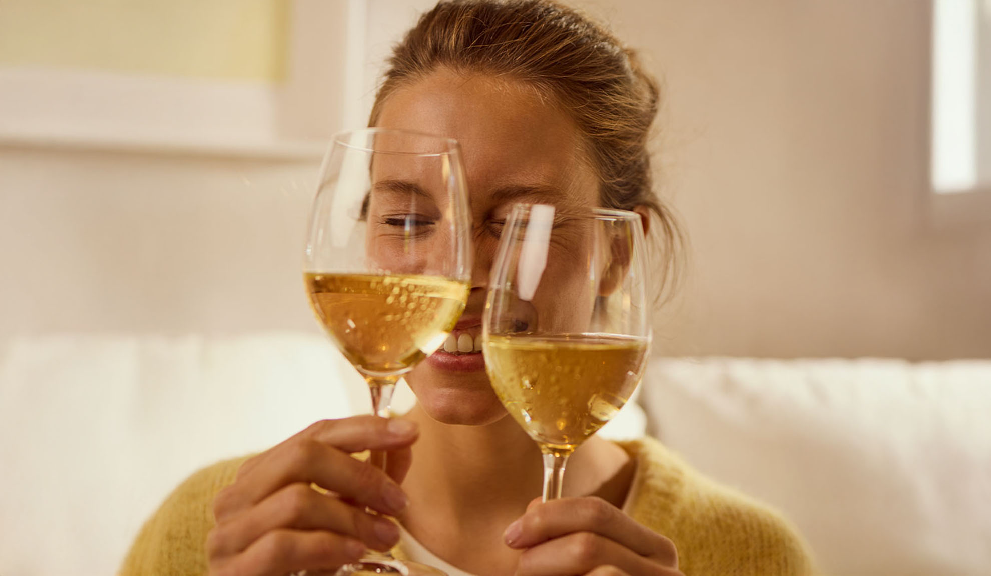 Lächelnde Frau hält zwei Gläser Weißwein.