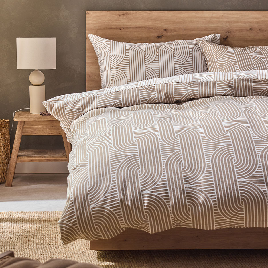Bettwäsche mit braun-weißem geometrischem Muster auf einem Holzbett.