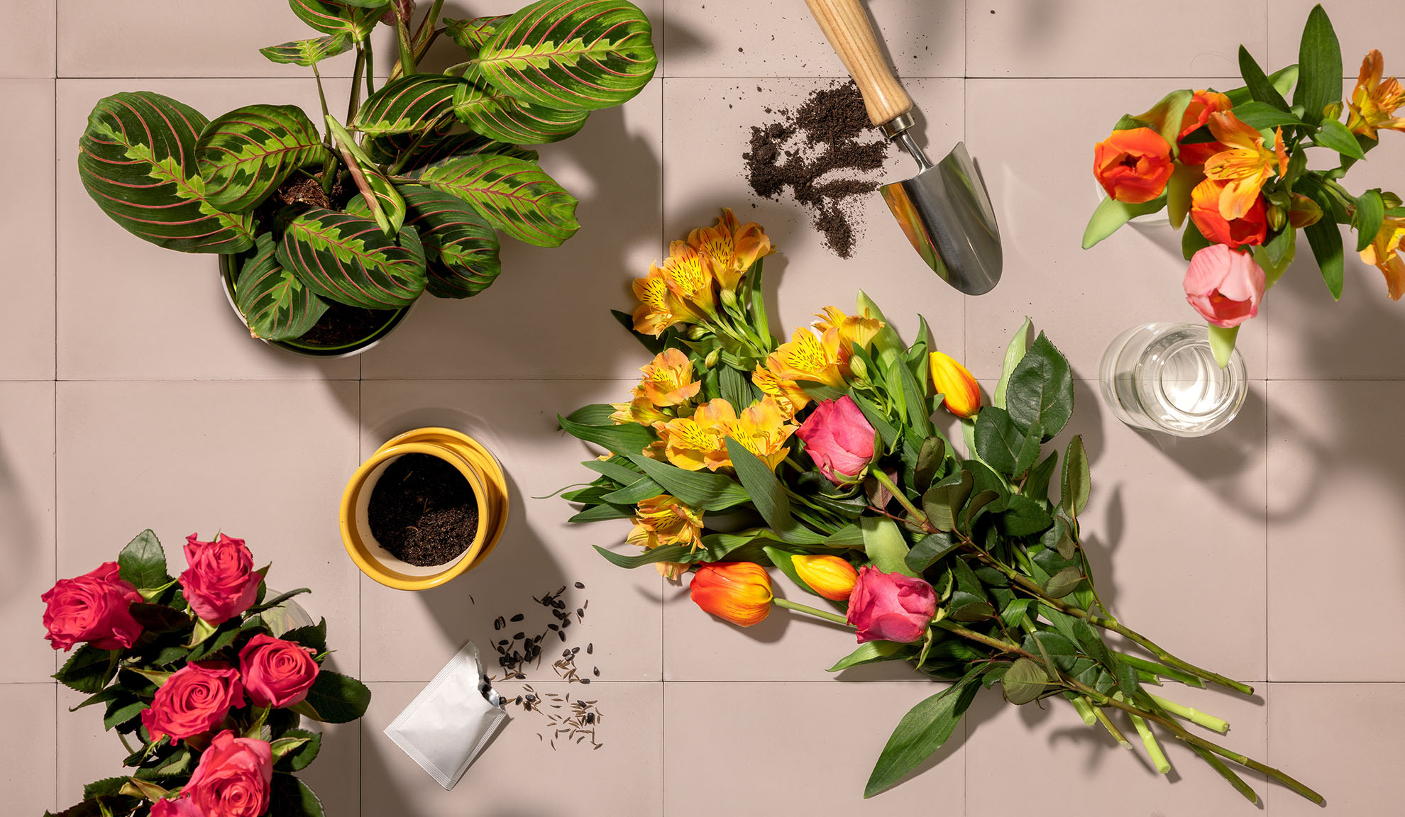 Draufsicht auf Gartengeräte, Topfpflanzen und bunte Blumensträuße auf einer gefliesten Oberfläche.