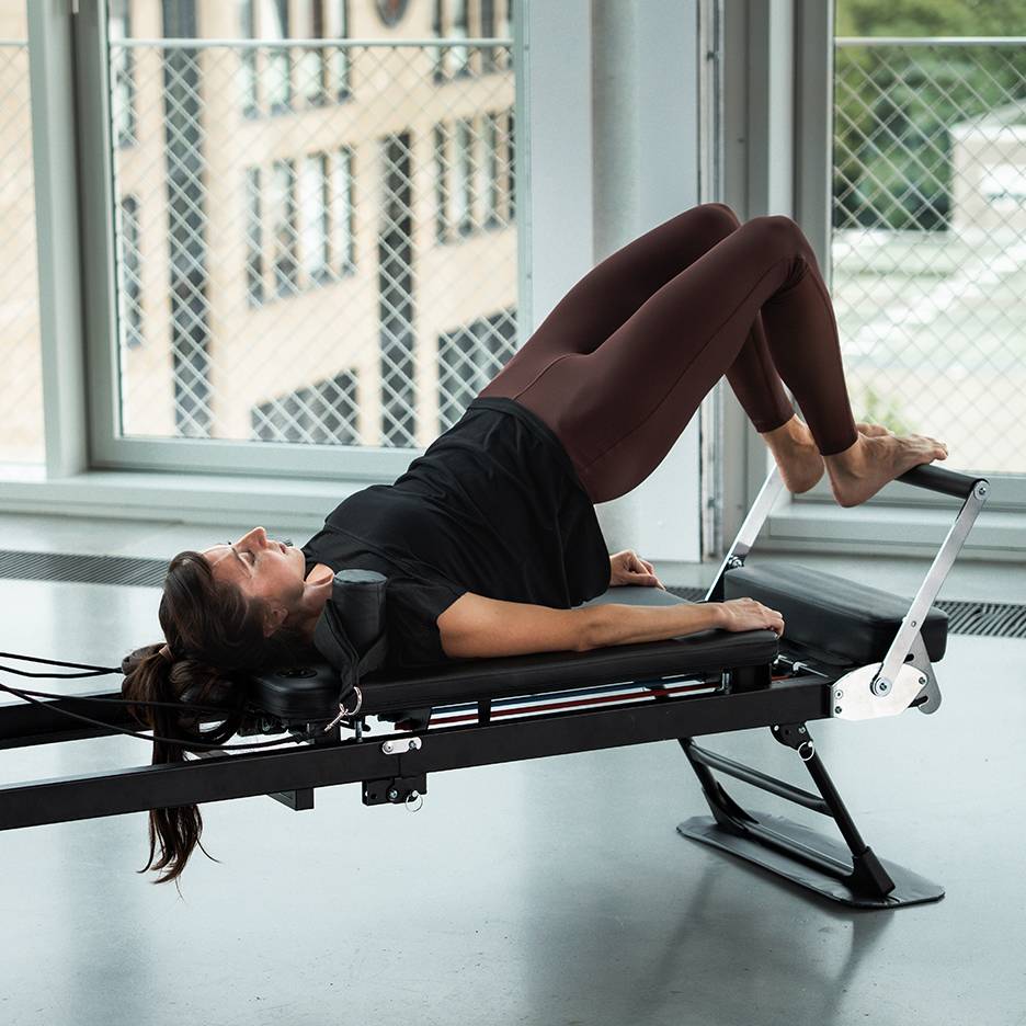 Frau macht Pilates auf einem Reformer-Gerät, Beine oben.
