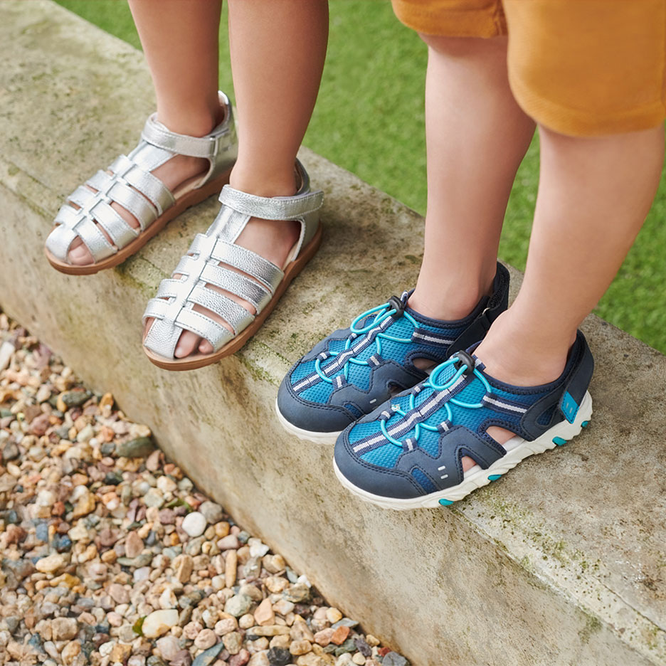 Zwei Paar Kindersandalen: silberne und blaue, auf einem Bordstein.