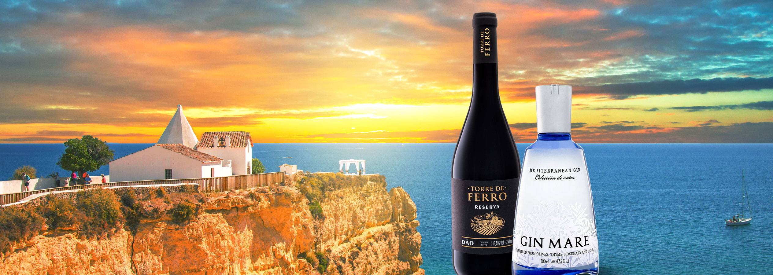 Rotwein und Gin vor einer Küstenlandschaft bei Sonnenuntergang.