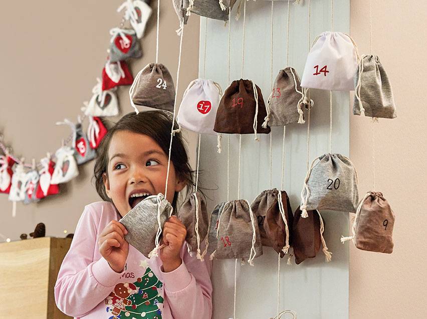 Mädchen mit Adventskalender: nummerierte graue und beige Stoffbeutel.