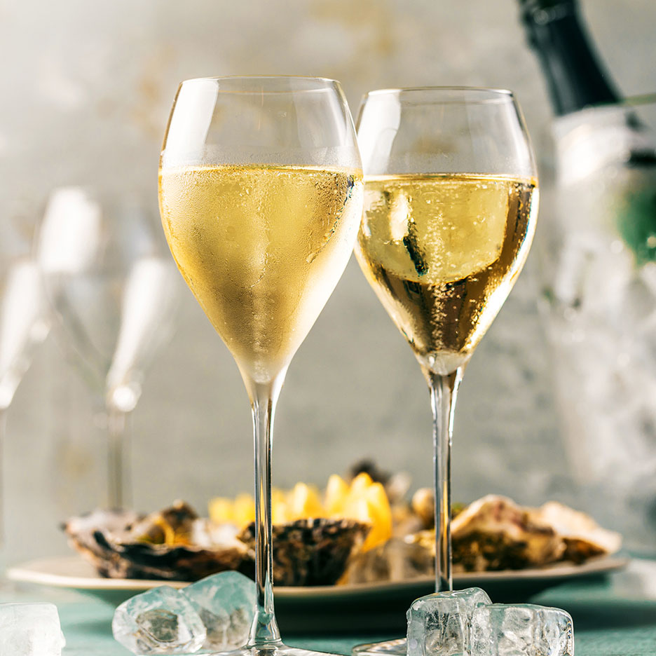 Zwei Gläser Sekt oder Champagner mit Austern und Zitrone im Hintergrund.