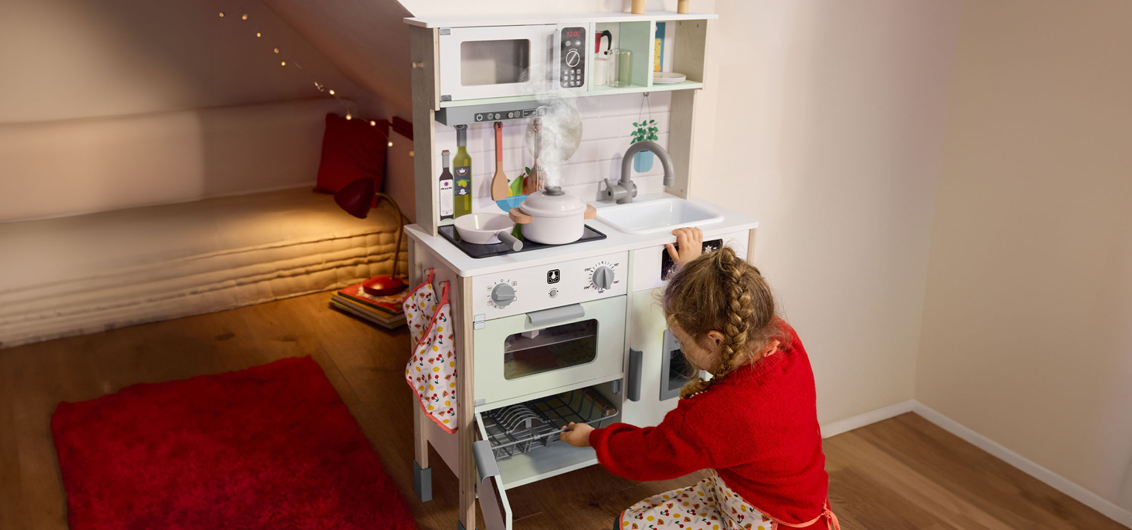 Zwei Kinder spielen in weihnachtlich dekorierten Räumen mit einer Spielküche und einer Spielzeugeisenbahn.