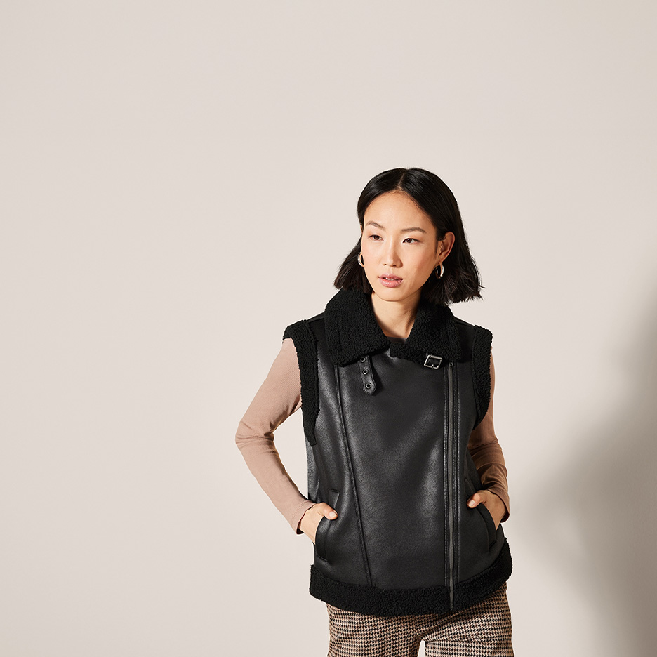 Frau in schwarzer Kunstlederweste mit Teddyfutter und beigem Langarmshirt